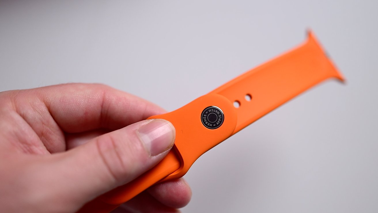 An orange sport band with a small Hermes logo on the metal pin