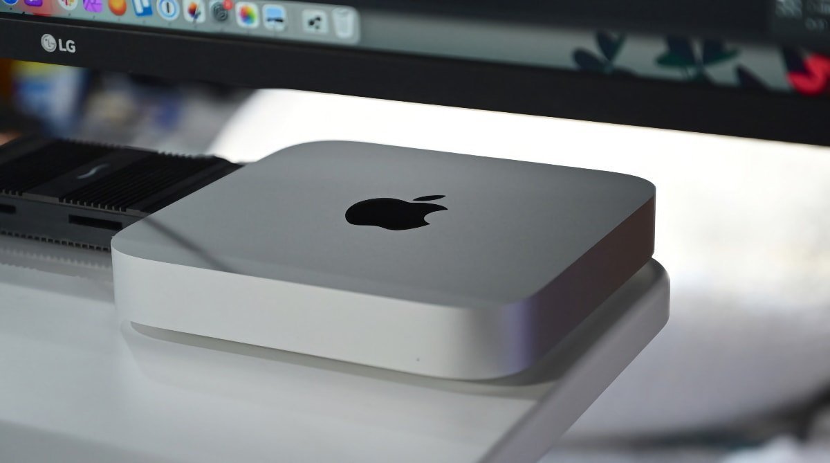 Silver Mac Mini computer below an LG monitor on a white desk.