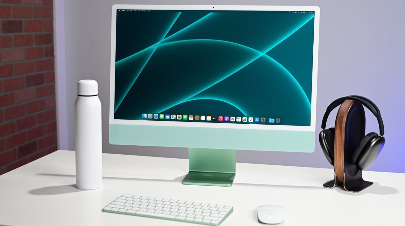 Desktop setup with a green computer, wireless keyboard, mouse, white water bottle, and headphones on a stand.