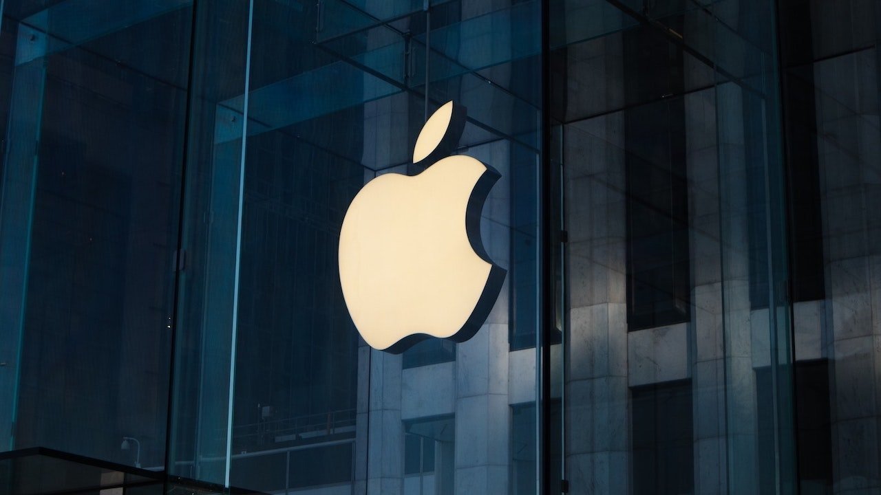 Large illuminated apple logo on a glass building facade, with dark reflections and vertical lines in the background.