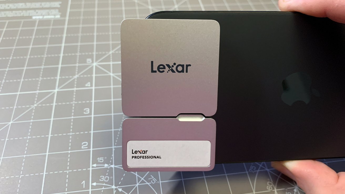 Hold the Lexar Professional memory card in front of the black device with the Apple logo and place it on the cutting mat with measurement marks.