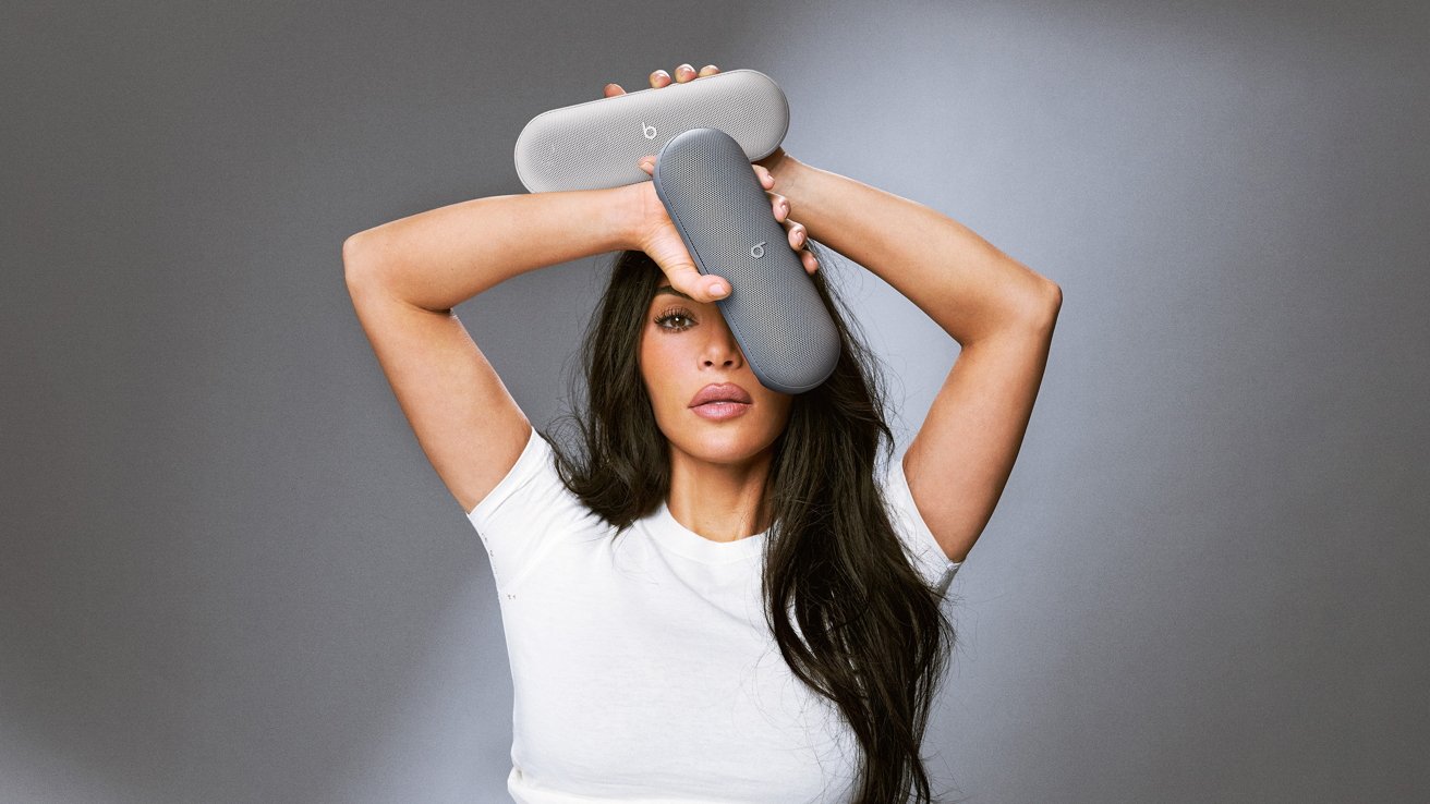 Person in a white shirt holding two gray speakers above their head against a neutral background.