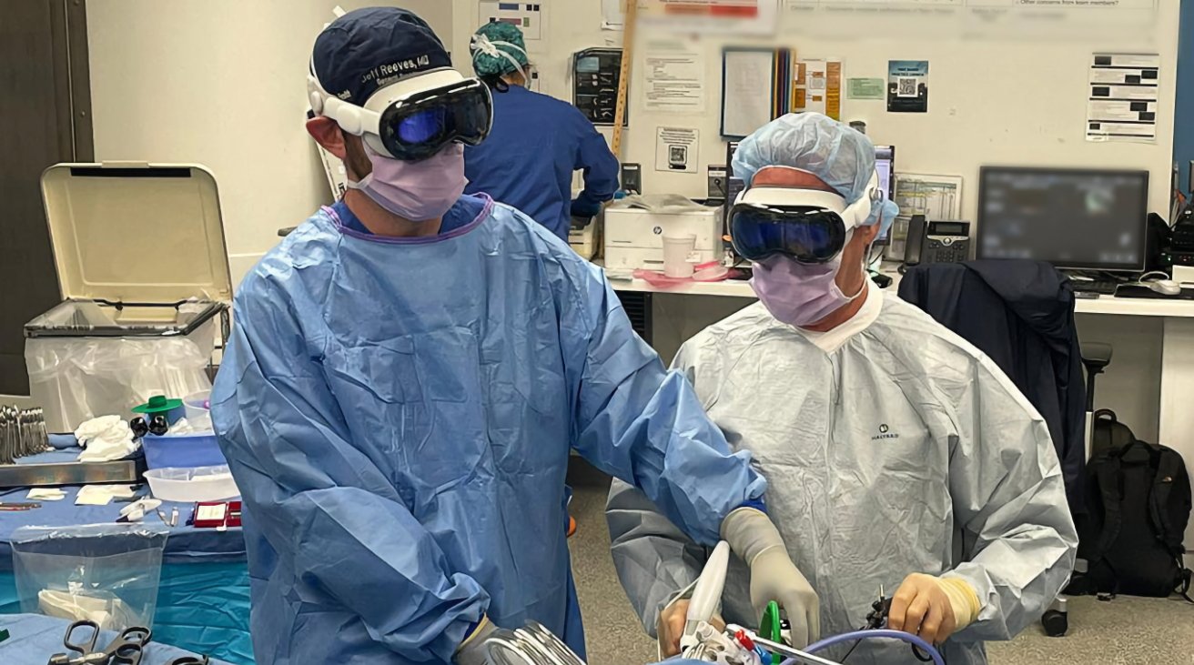 Two surgeons wearing blue scrubs and augmented reality headsets work in an operating room filled with medical equipment.