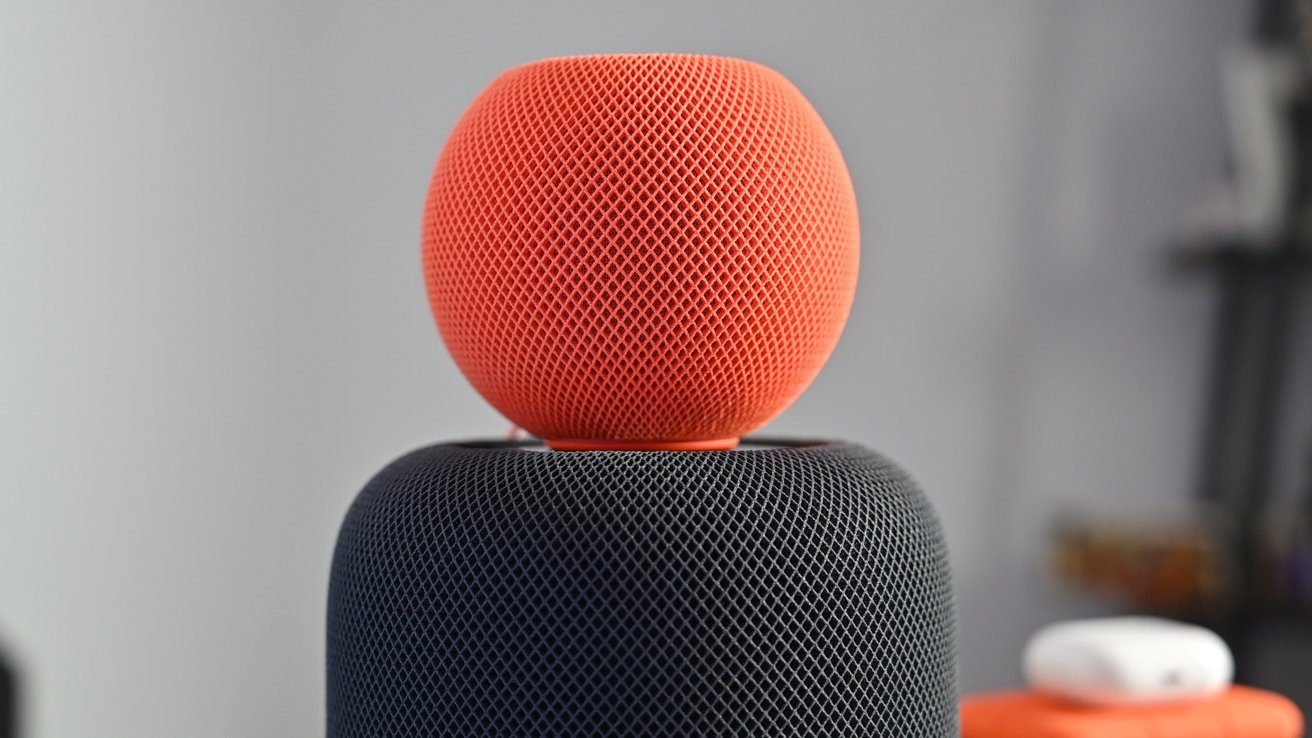 Two HomePod speakers, one orange and one black, stacked on top of each other against a blurred background.