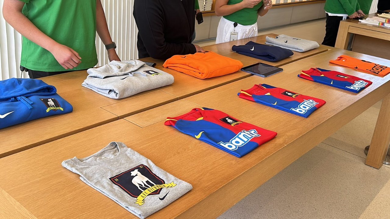 Folded sports jerseys and hoodies displayed on a wooden table, with people standing nearby.