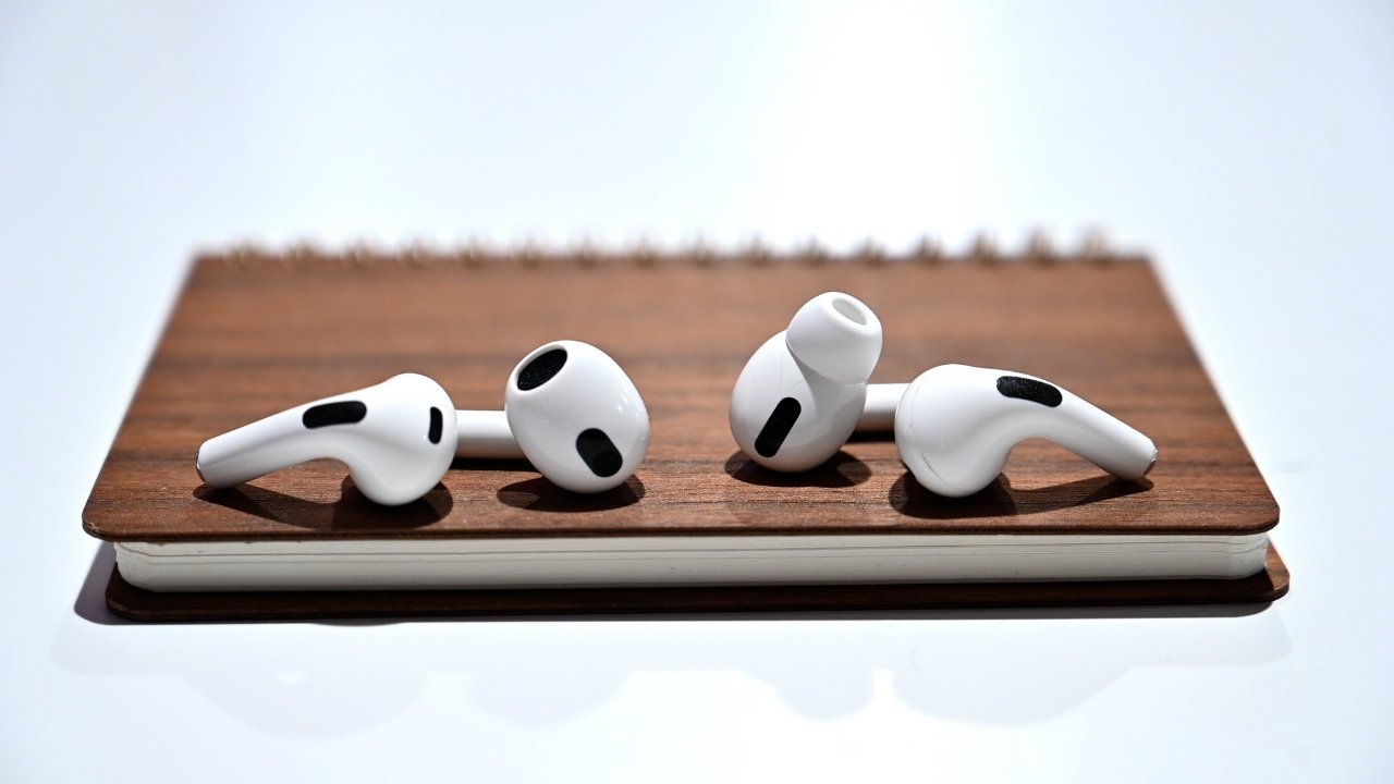 Four white wireless earbuds with black accents resting on a closed brown notebook with a white edge.