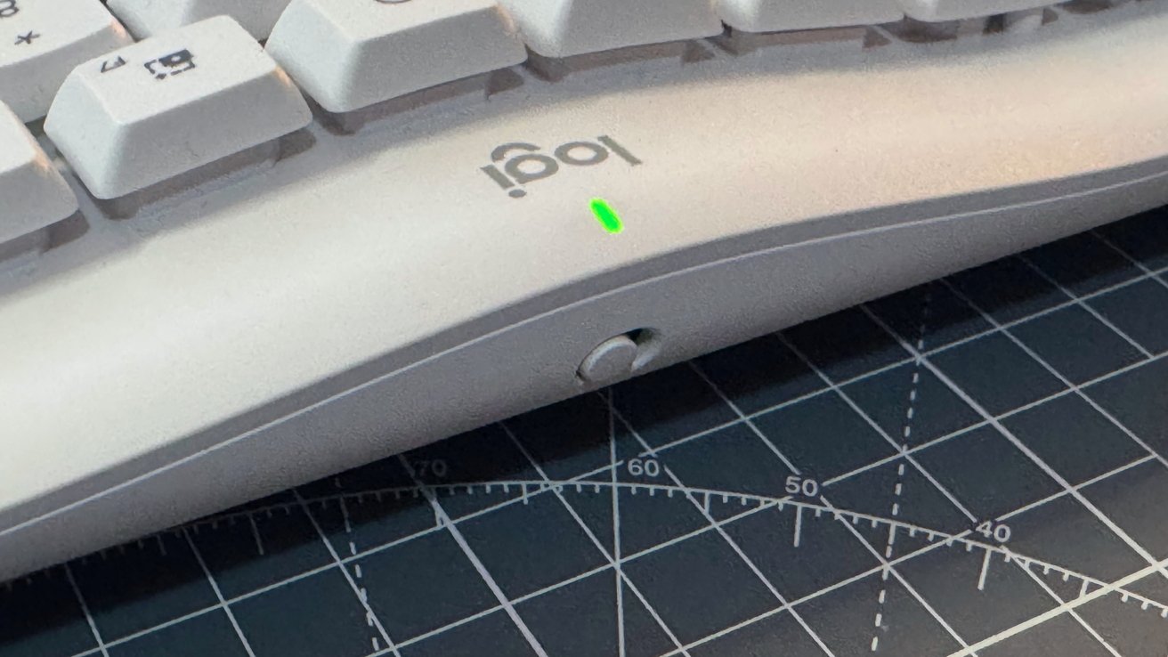 White computer keyboard with green light, placed on a black and white grid cutting mat.