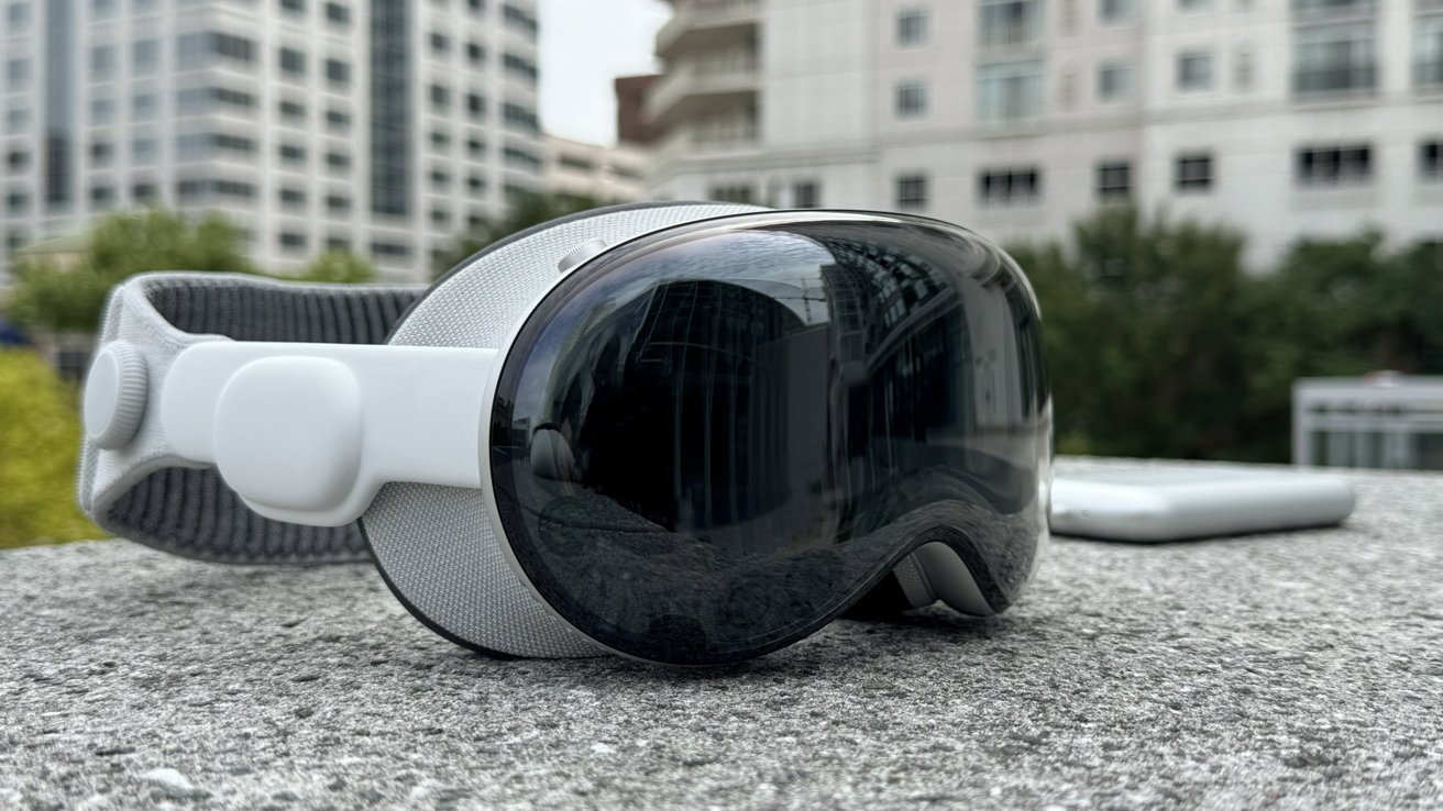 A high-tech virtual reality headset with reflective goggles rests on a concrete surface, with buildings in the blurry background.