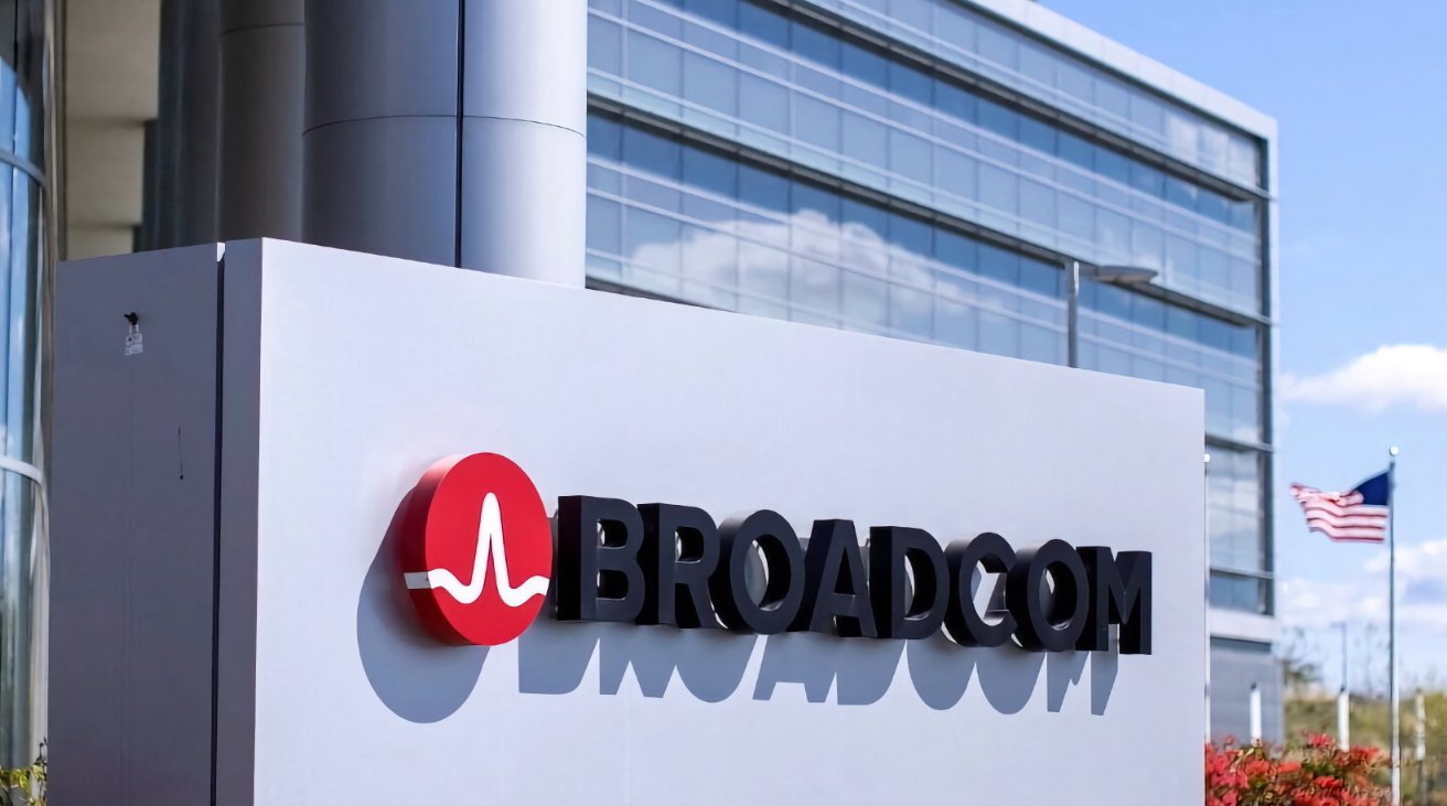 Broadcom logo on a gray sign in front of a modern office building with reflective glass windows and an American flag.