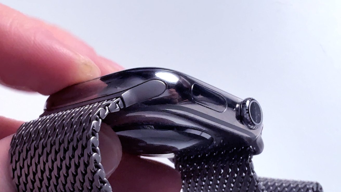 Close -up of a hand that holds a smart trip with a metal net band, side view showing the digital crown and the button.