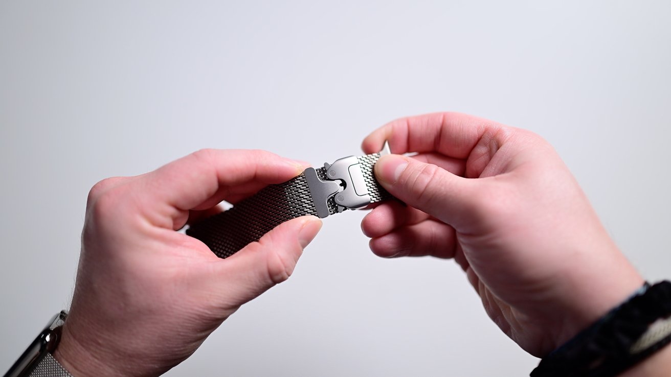 Hands that hold and adjust a stainless steel clock band with a locking mechanism, against a common background.