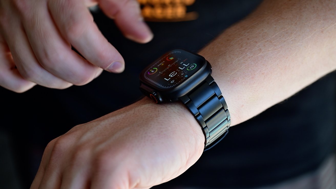 Person wearing a smartwatch with a black metal band, touching the screen with their other hand.