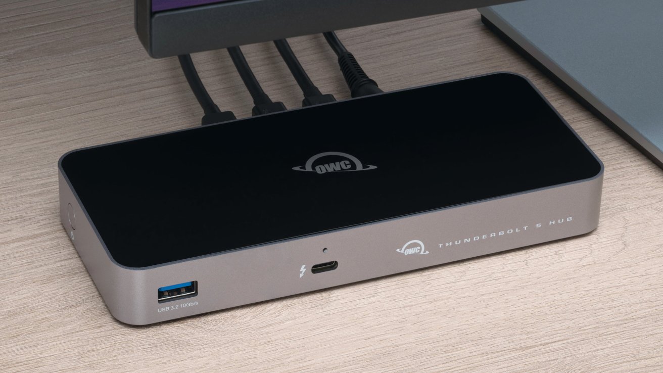 A sleek OWC Thunderbolt 5 Hub with multiple cables connected, resting on a wooden surface, featuring USB and Thunderbolt ports.