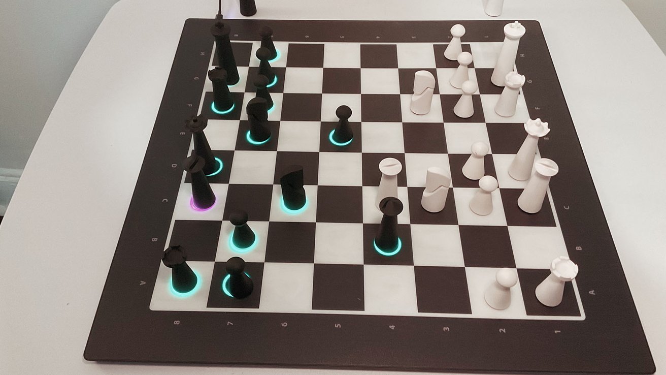 Chessboard with black and white pieces. Some pieces have glowing bases in turquoise and purple, possibly indicating active or selected. The board is on a white table.