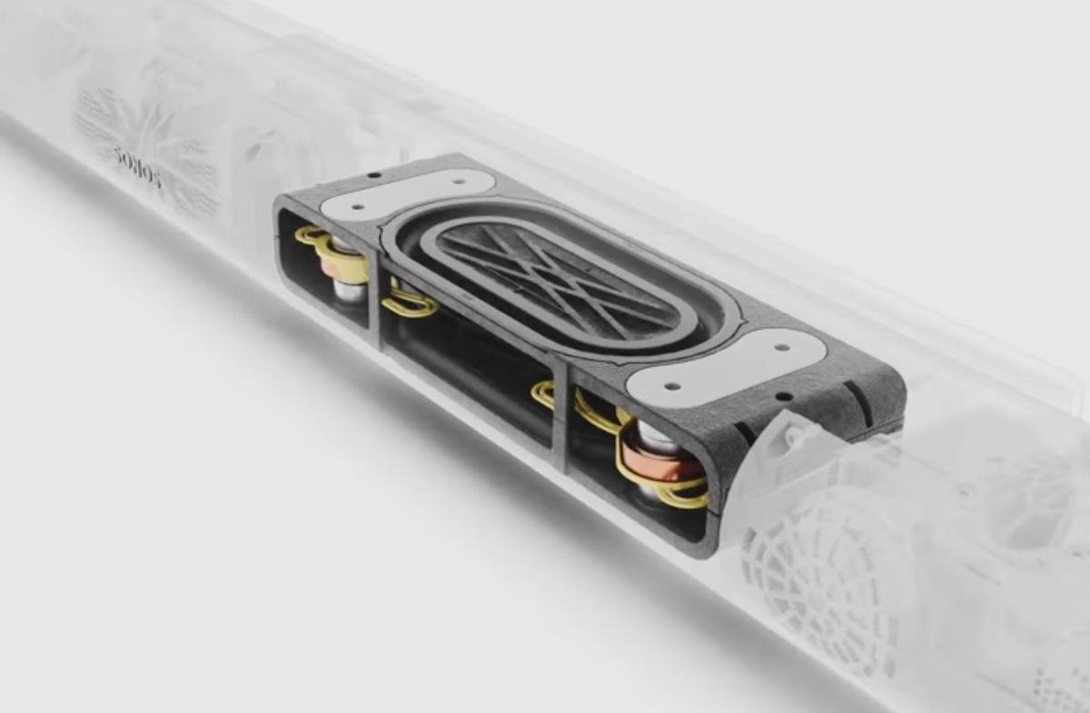 Transparent speaker casing revealing internal components, including an oval speaker driver and circular elements, on a light gray background.