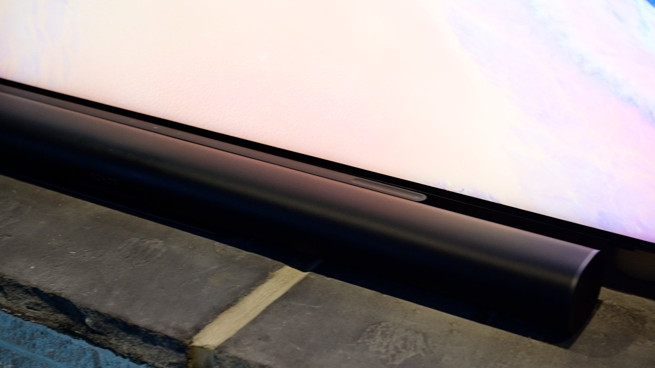 Close-up of a slim black soundbar placed below a large screen on a stone surface.