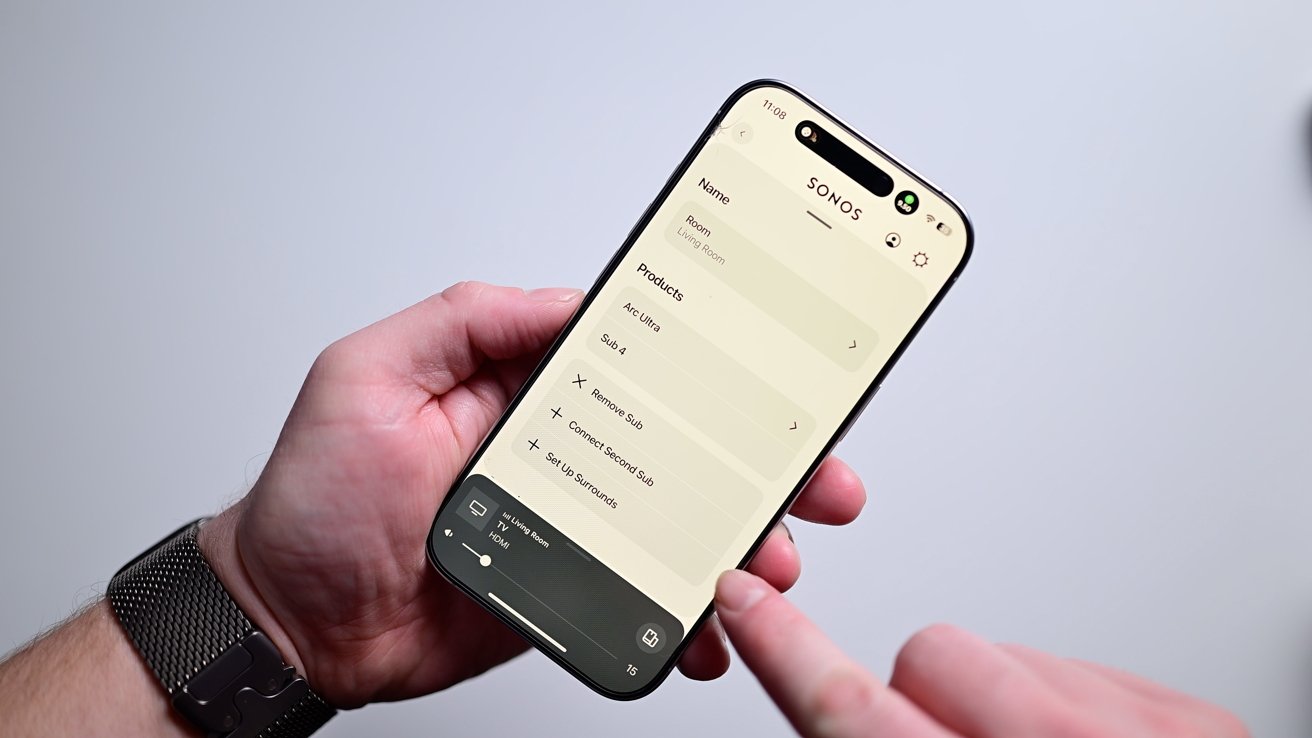 Person holding a smartphone displaying the Sonos app with settings for Arc Ultra, Sub 4, and various connection options.