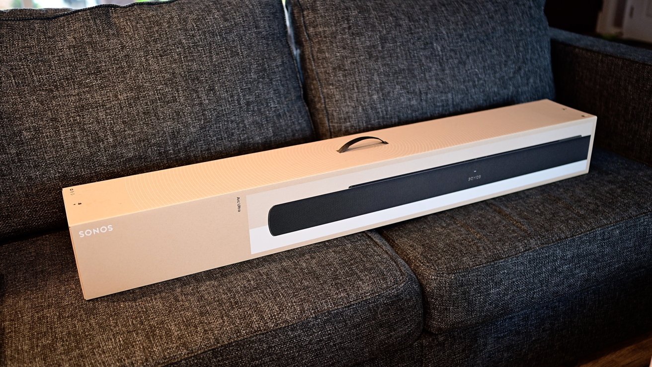 A long beige box labeled Sonos placed on a gray sofa.