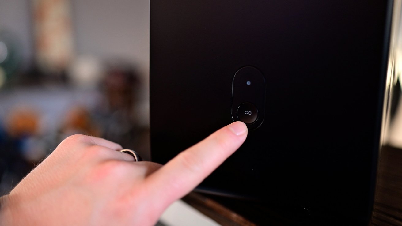 A finger pressing a button with an infinity symbol on a black surface, with a blurred background.