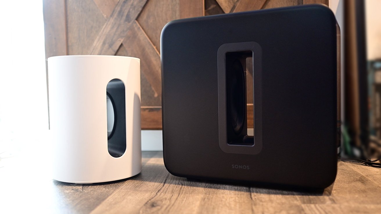 White and black rectangular speakers with oval cutouts on a wooden surface, set against a textured wooden background.