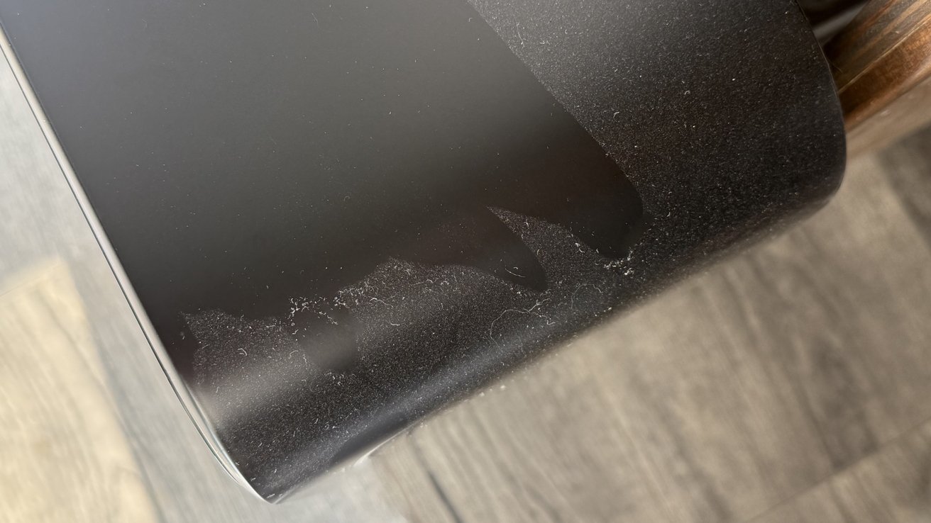 Close-up of a black surface with peeling material and dust, next to a wooden floor.