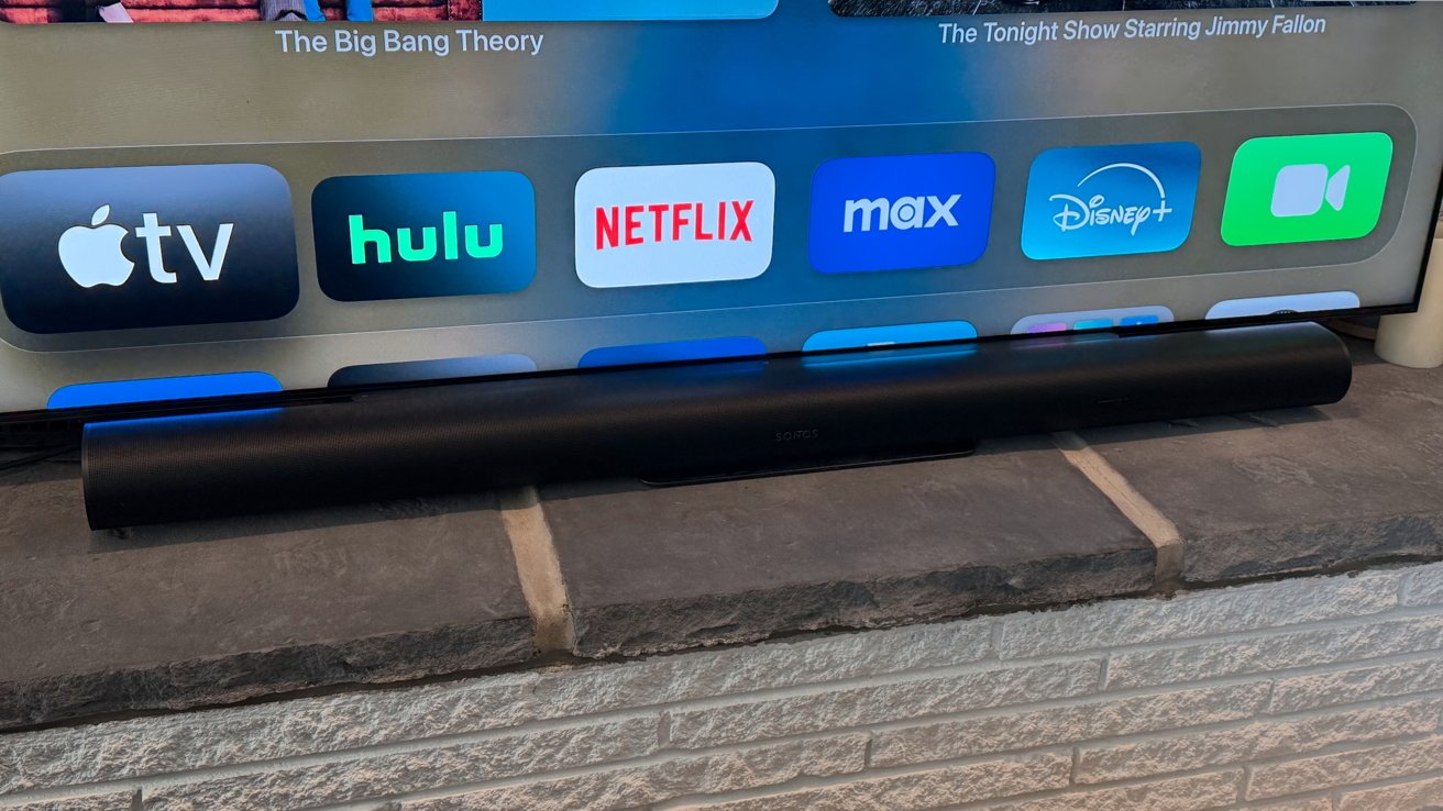 Television screen displaying streaming apps like Apple TV, Hulu, Netflix, and Disney+ above a black Sonos soundbar on a stone surface.