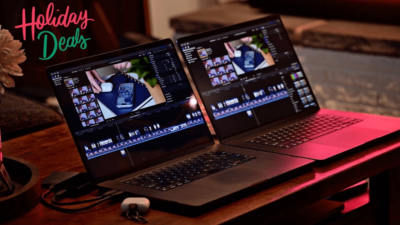 Two MacBook Pro laptops displaying video editing software on a wooden table with a holiday deals sign in the corner, alongside a small white object.