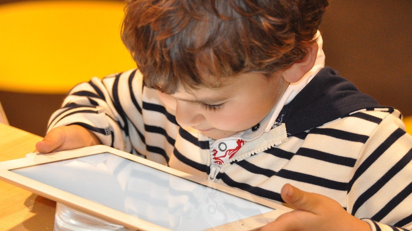 Child in striped sweater closely looking at a tablet screen with focused expression.