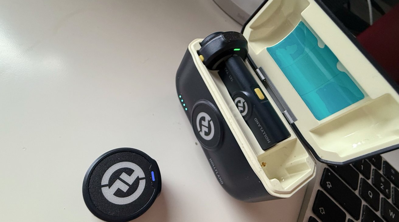 Open black and white electronic case with glowing LEDs on a desk, containing two cylindrical devices, next to a circular black accessory with a logo.