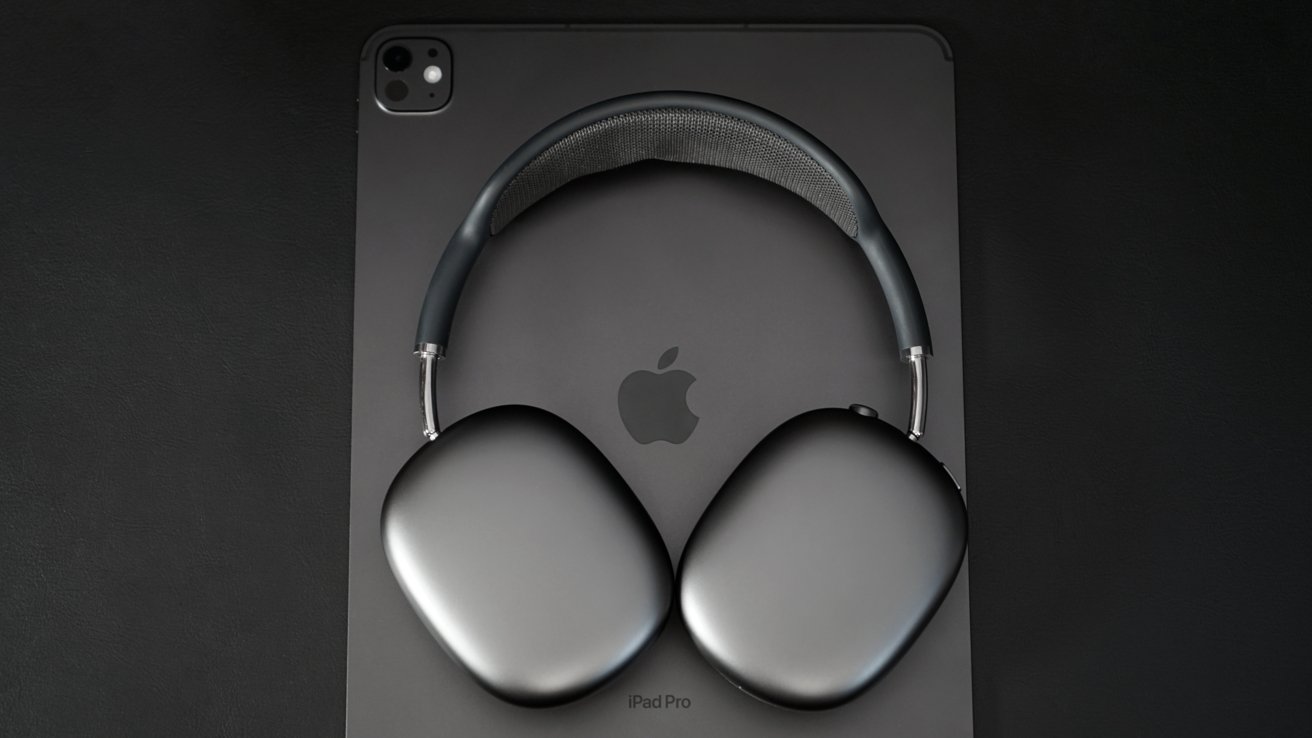 Black over-ear headphones resting on a dark gray tablet with an Apple logo, on a black background.