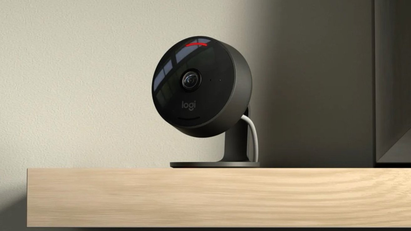 A black security camera with a round lens is mounted on a wooden shelf, with a white wire extending from it.