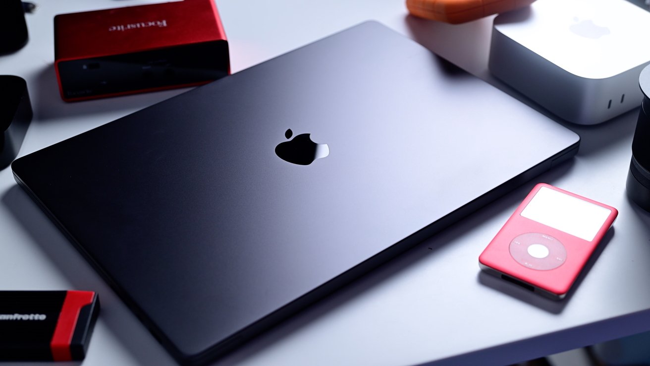 Closed laptop with Apple logo, red portable media player, red and gray external boxes, and various electronic devices on a white surface.