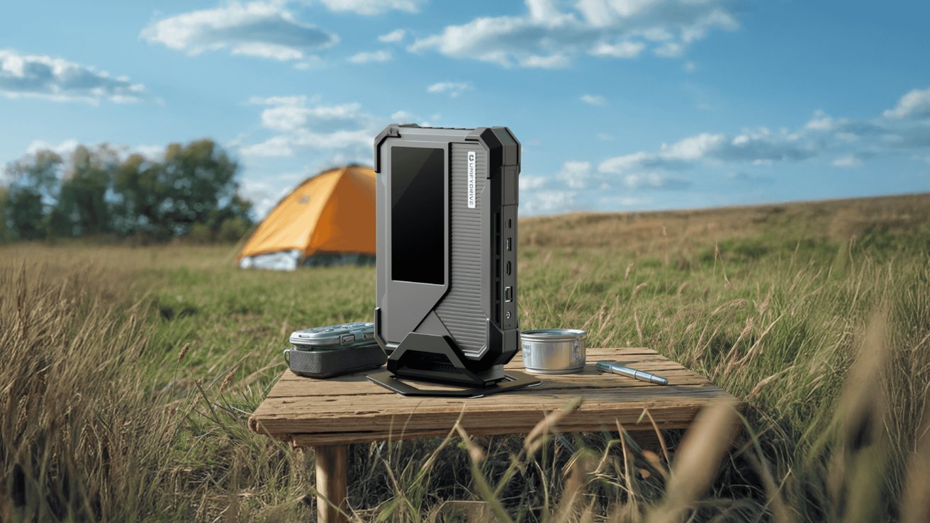 A rugged outdoor power bank on a wooden table in a grassy field with an orange tent and blue sky.