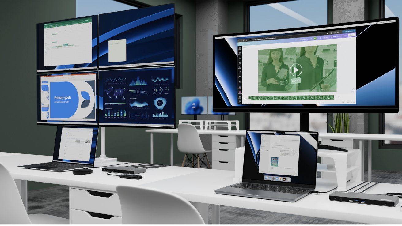 Office with multiple computer monitors displaying graphs, spreadsheets, presentations, and a video. Laptops, a docking station, and white chairs are arranged on desks near large windows.