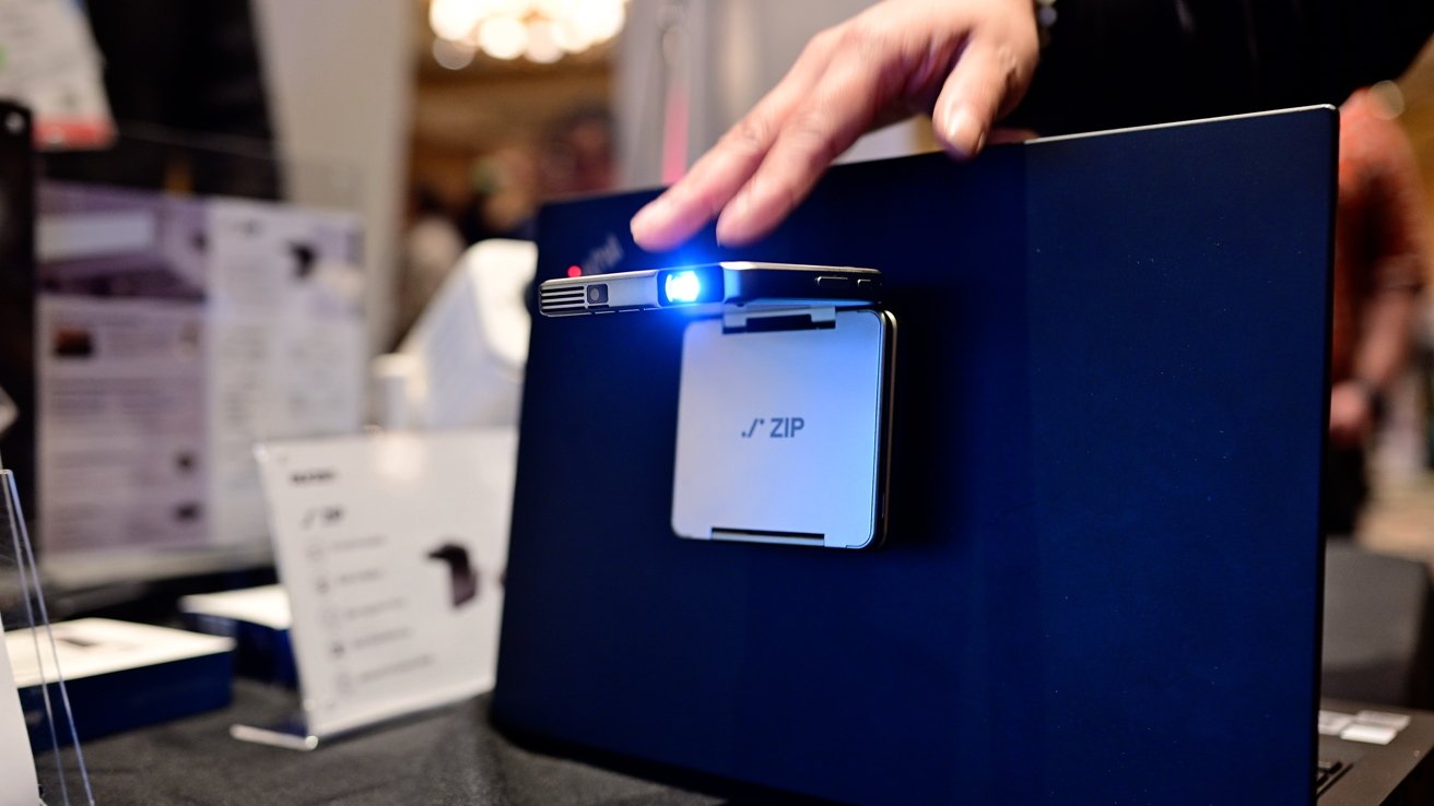 A hand hovers over a small blue-lit projector mounted on a dark surface with a 'ZIP' label.