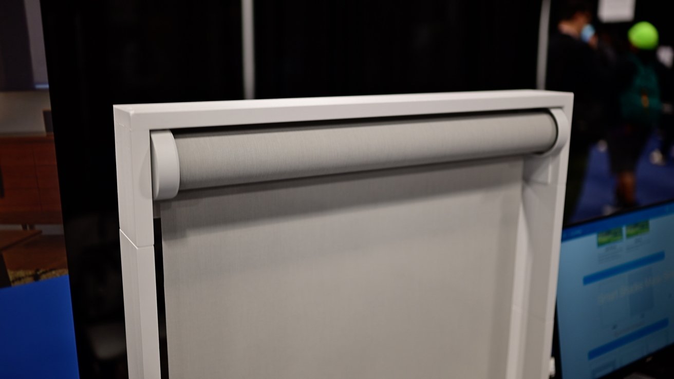 White framed window blind with gray fabric, partially rolled down, against a dark background.