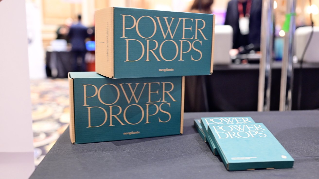 Two teal boxes and two teal booklets labeled 'Power Drops' are on a black table with a blurred background.