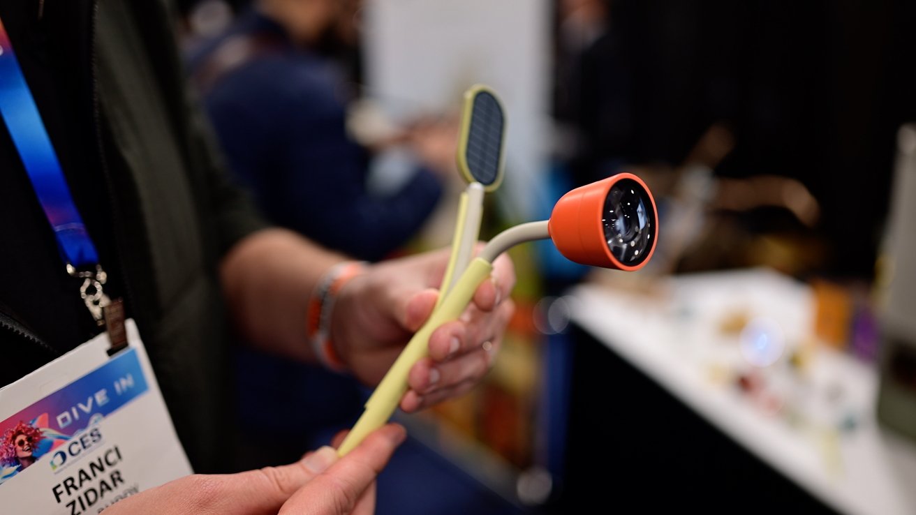 Person holding a flexible tool with a red camera-like device and a small solar panel.