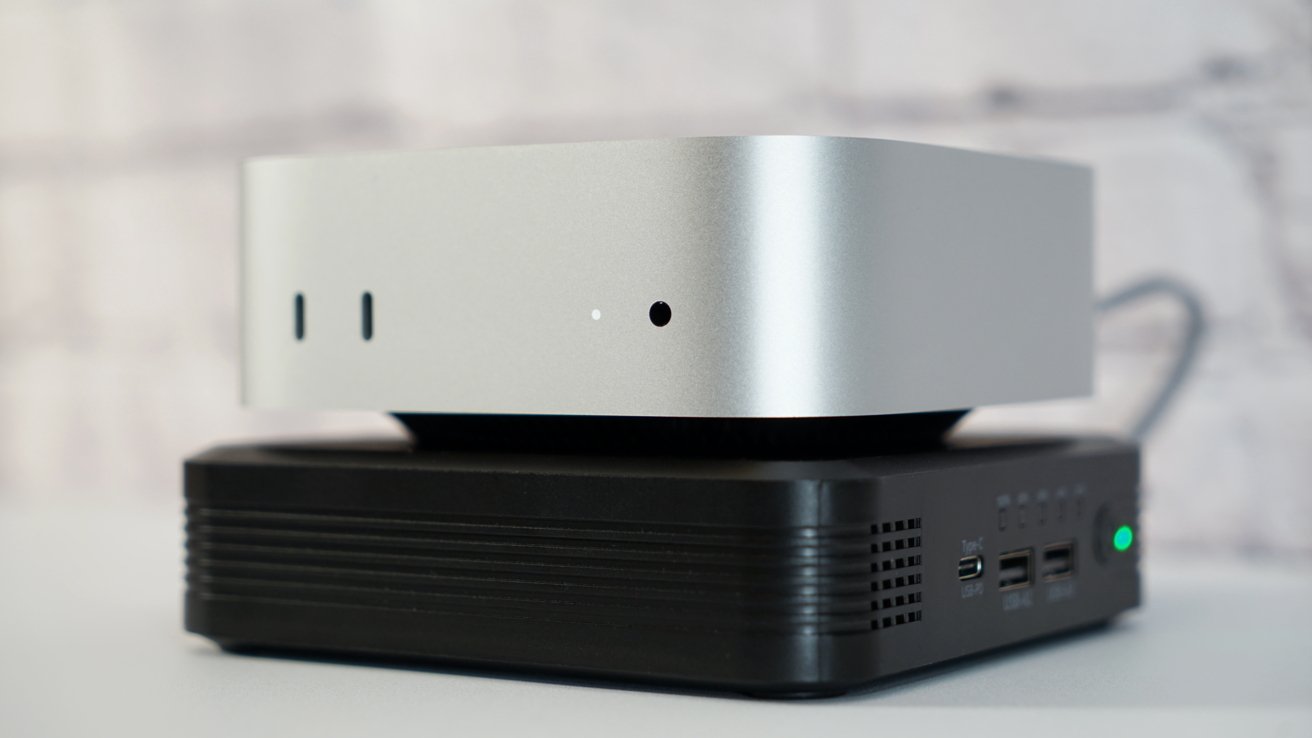 A silver electronic device sits atop a black base with USB ports and a green indicator light in a softly lit room.