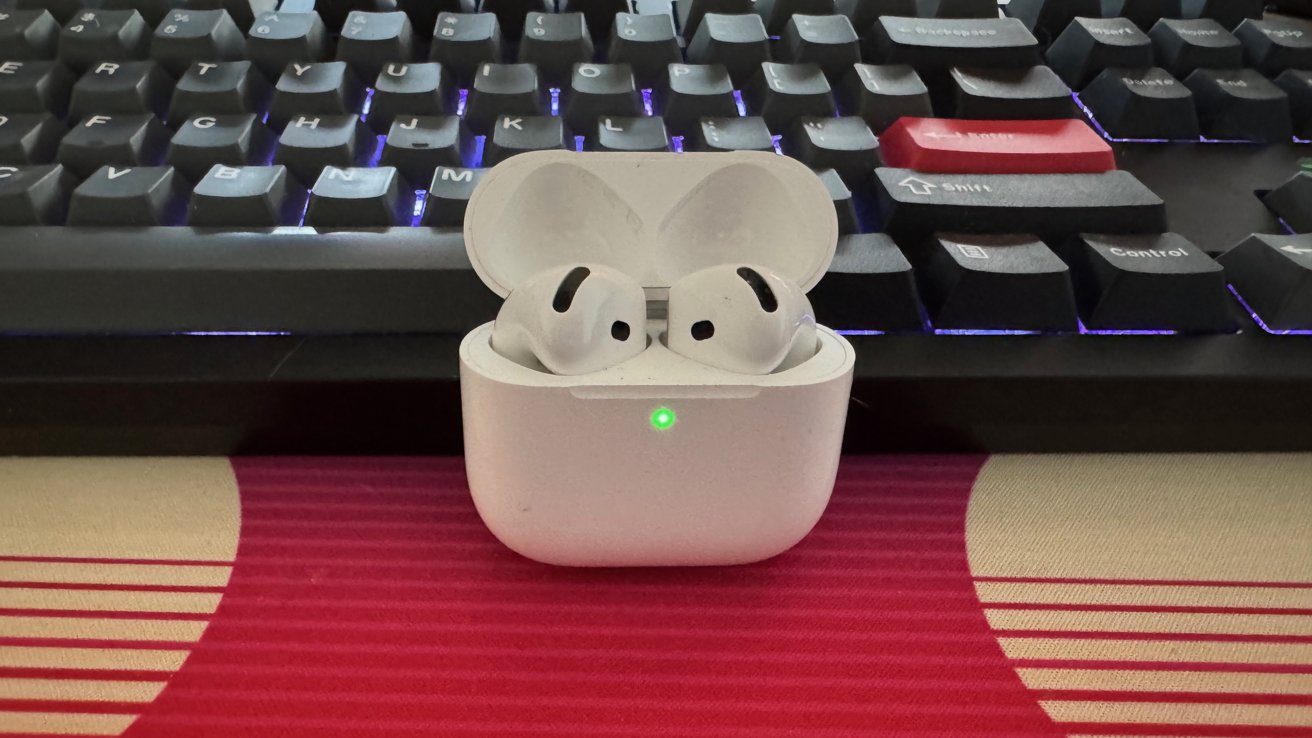 AirPods 4 in charging case with lid open, leaning against a keyboard.