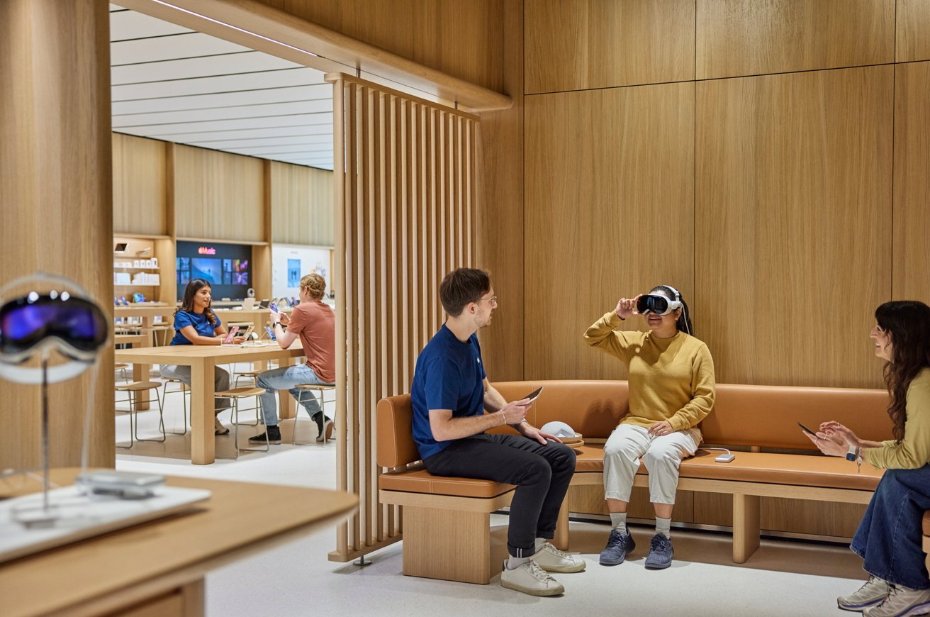 People in a modern store setting; one person wearing VR headset, others seated nearby engaged with tablets. Wood-paneled walls and tech displays in the background.