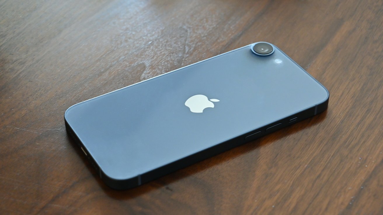 Smartphone with single rear camera and Apple logo, placed face down on a wooden surface.