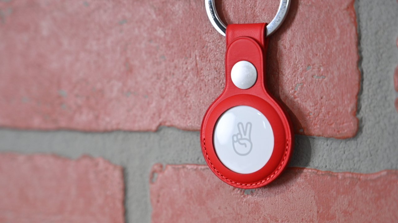 Red keyring attached to a brick wall, featuring a white circular device with a peace hand symbol in the center.