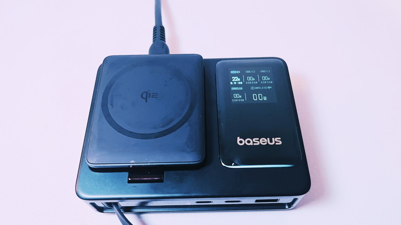 A black wireless charger with a digital display showing charging details and a plugged-in cable on a light surface.