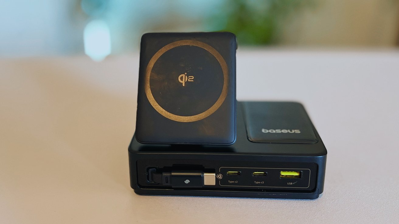 A black wireless charging station with a gold circular logo on the front, featuring multiple USB ports labeled Type-C and USB.