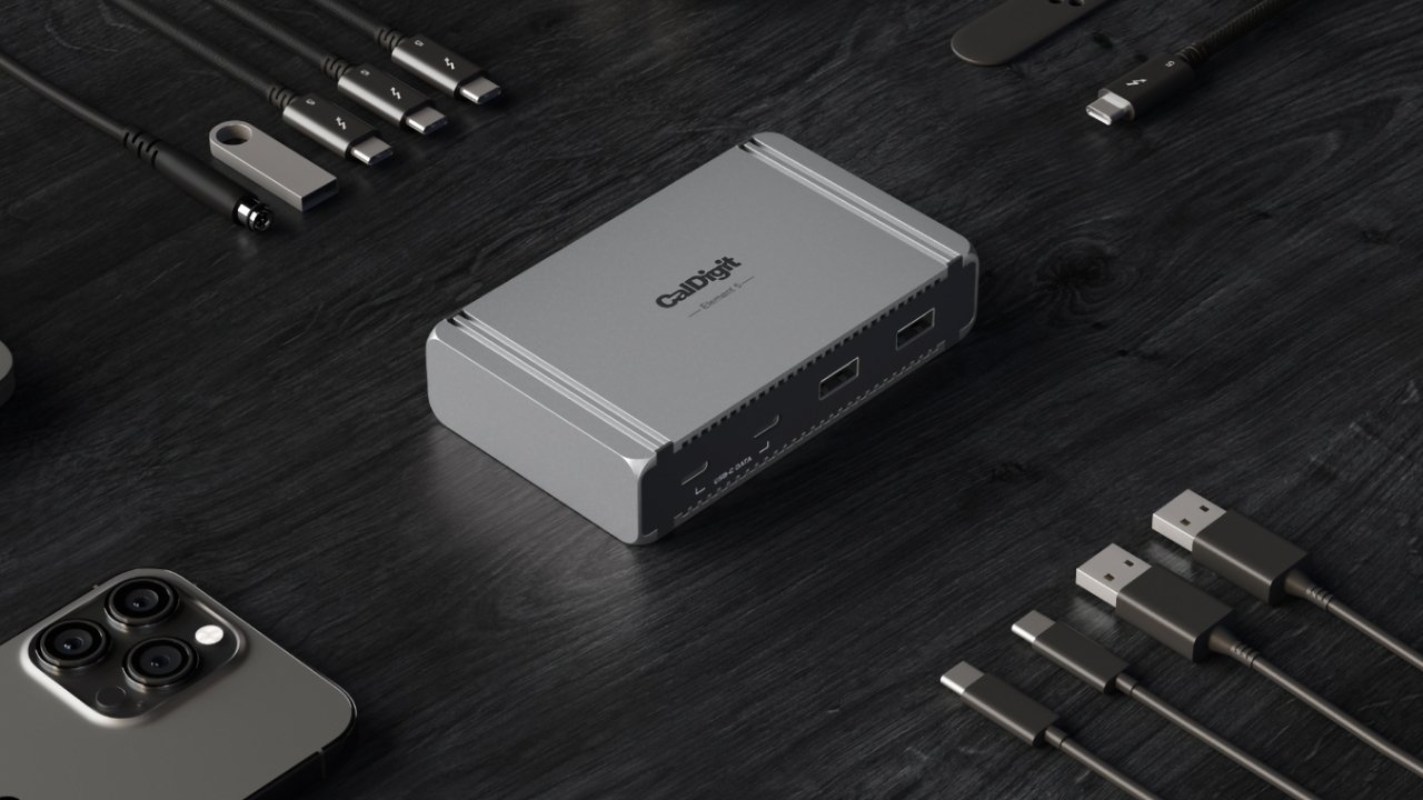 Silver electronic dock with multiple ports surrounded by various cables and a smartphone on a dark wooden surface.