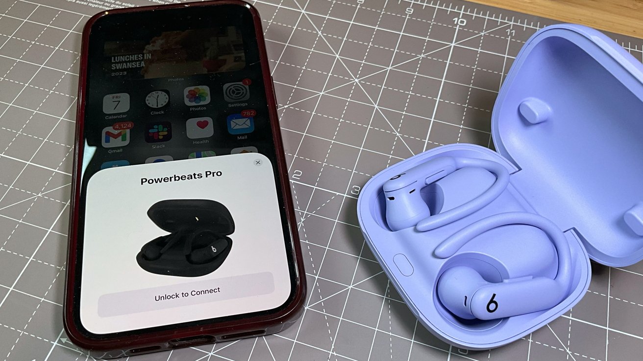 Smartphone displaying Powerbeats Pro connection prompt next to open lavender earphones case on a grid-lined surface.