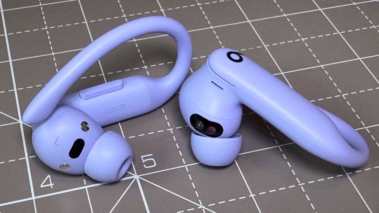 Two lilac wireless earbuds with hooks resting on a grid-patterned surface displaying numbers.