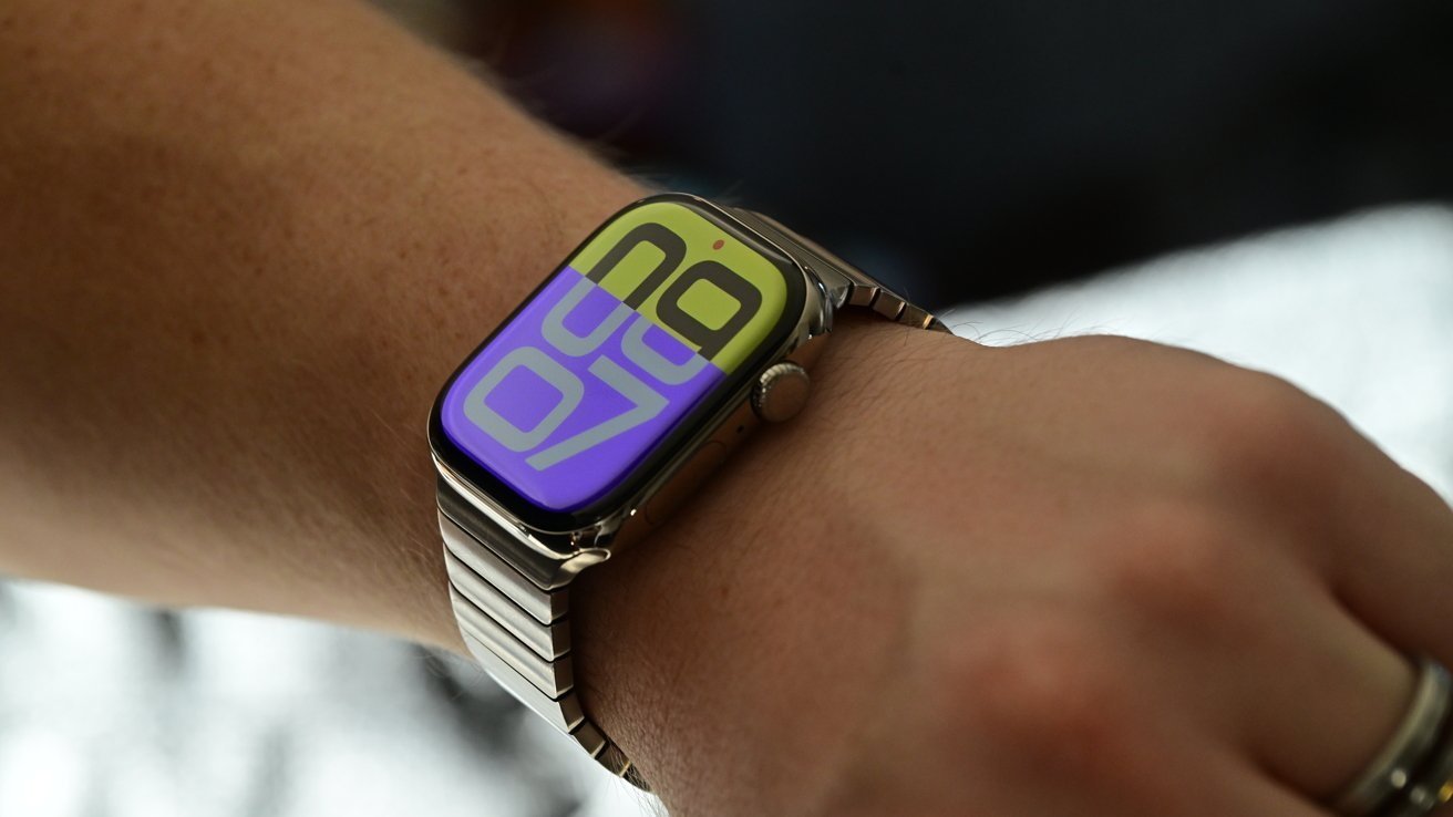 Smartwatch on wrist with large, colorful digital display showing time. Stainless steel band and a dark background.