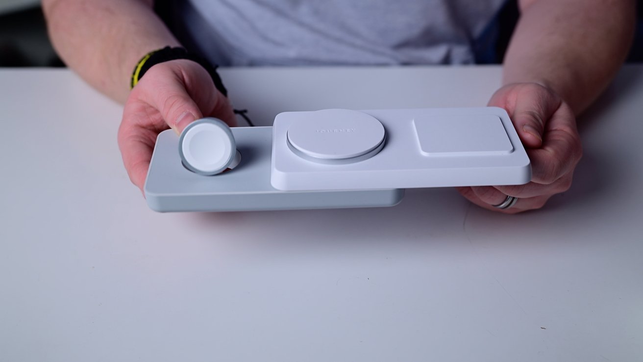 Person holding a white rectangular charging station with three circular charging pads on a table.